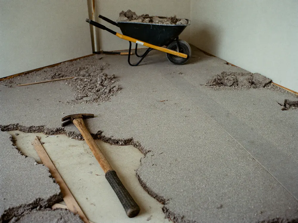 Een oude zandcement dekvloer is opgebroken, met een kruiwagen vol puin