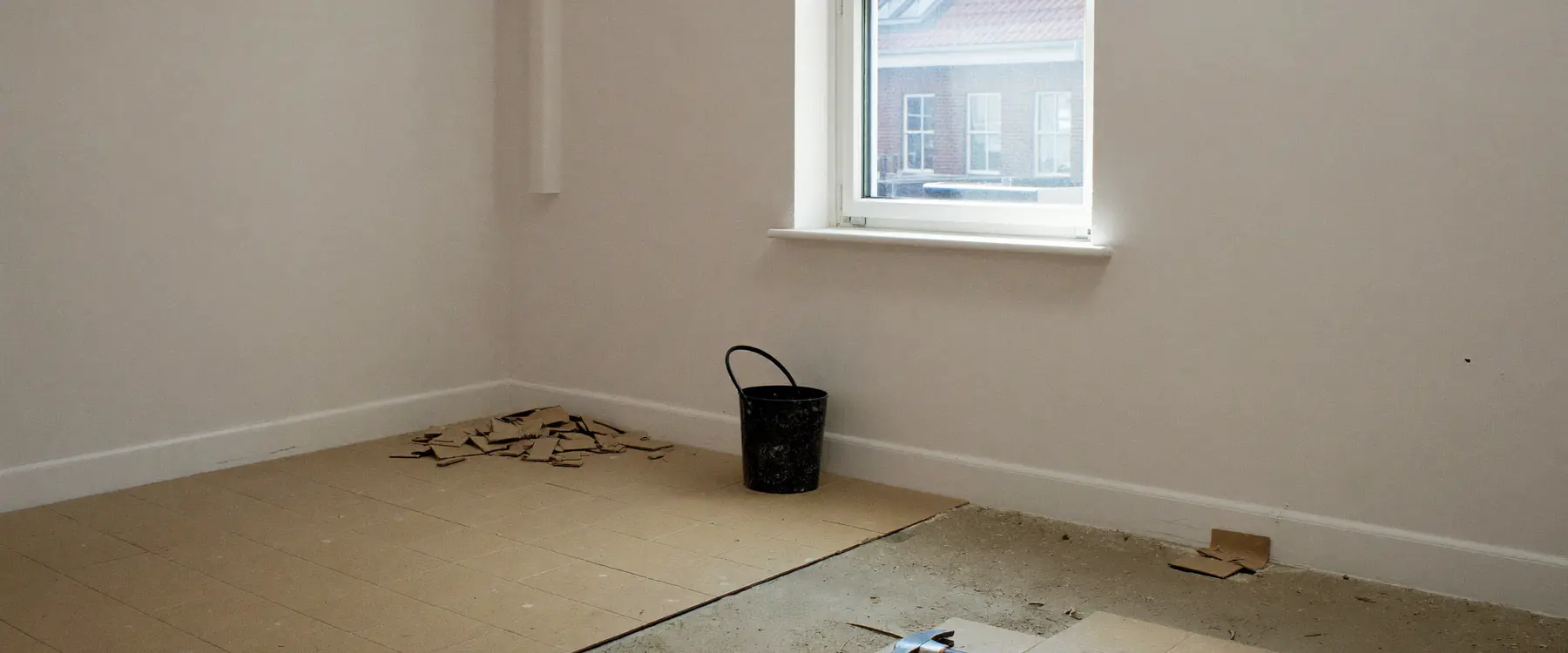 Woonkamer waarin de oude tegelvloer half is verwijderd en de dekvloer met lijmresten zichtbaar is
